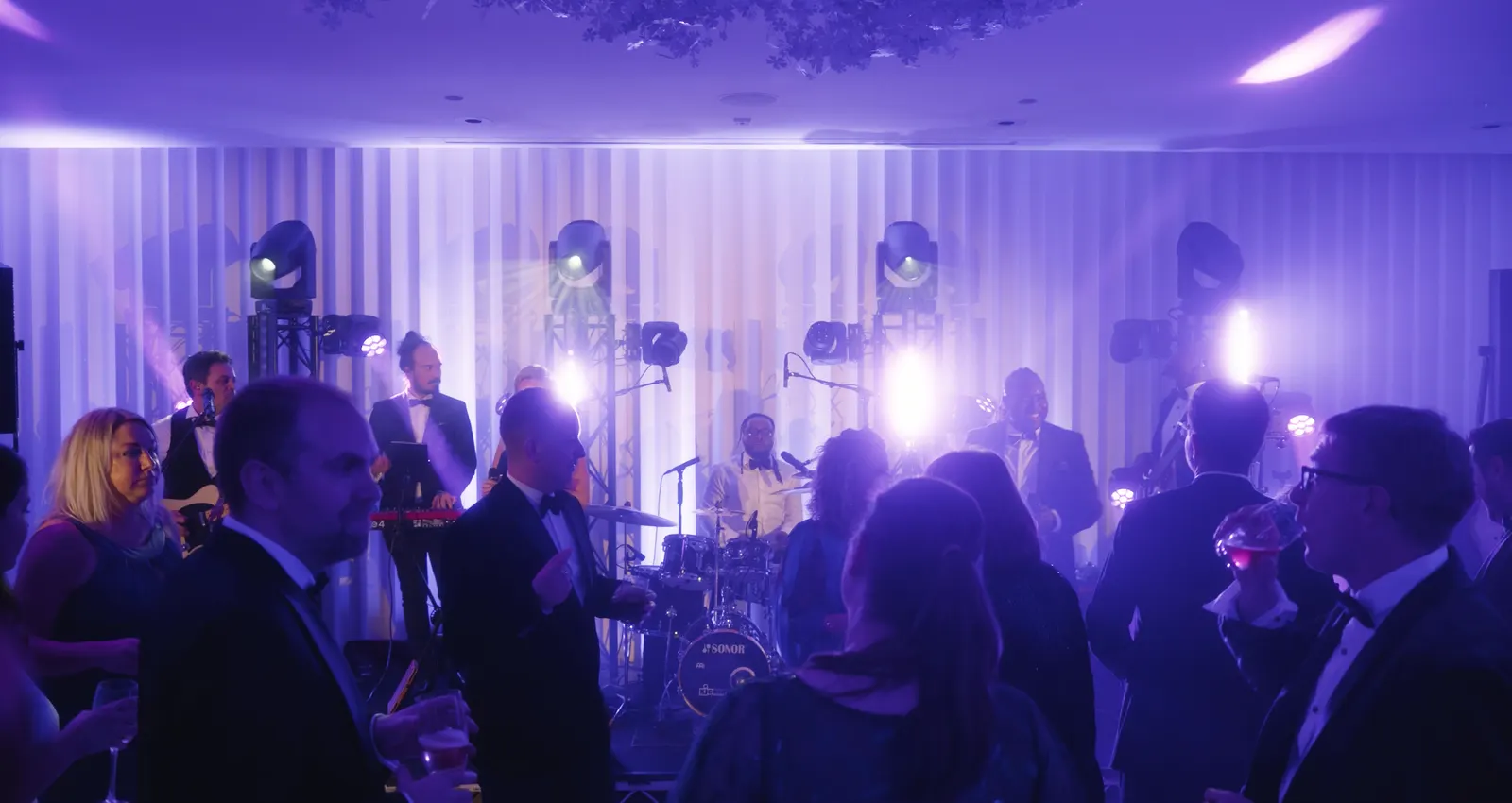 A live band playing to guests in a hotel ballroom with moving heads on truss and a tuned PA