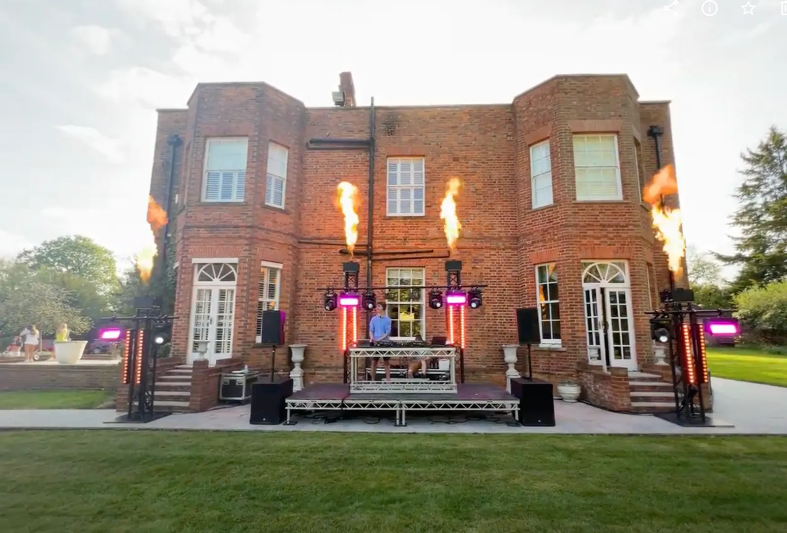 Garden DJ stage at a private 21st in Berkshire: truss towers with moving heads, LED battens and flame jets in front of a brick house at dusk