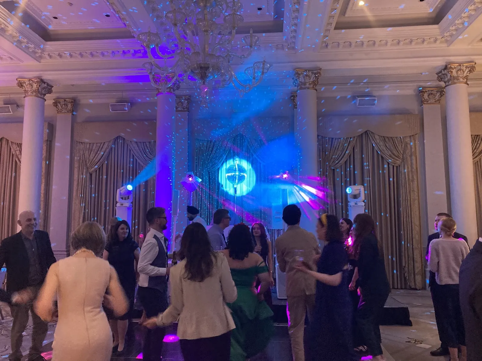 Guests dancing in a hotel ballroom under a chandelier, with moving heads, a mirror ball and light haze