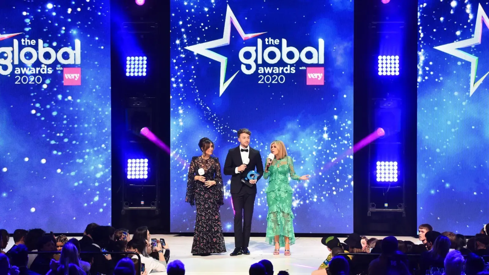 Presenters on the Global Awards 2020 stage in front of a large LED wall with moving lights on towers either side