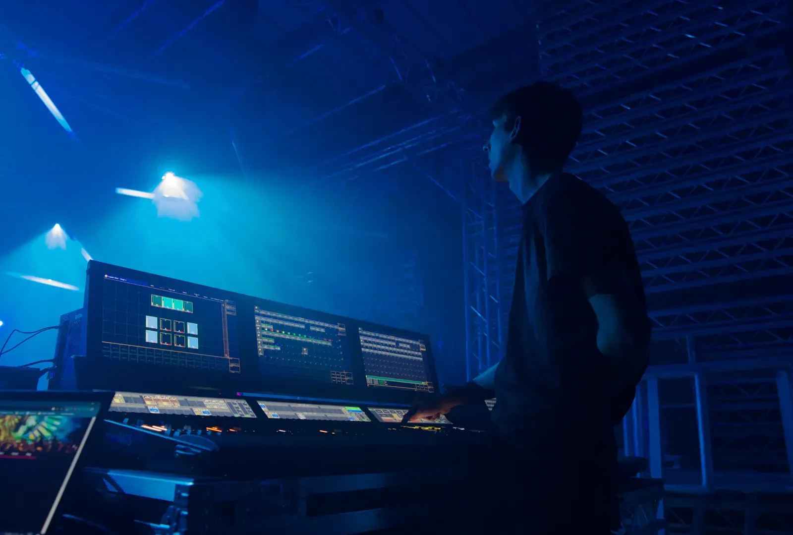 A lighting operator at a grandMA3 console with haze and moving lights in the rig behind him
